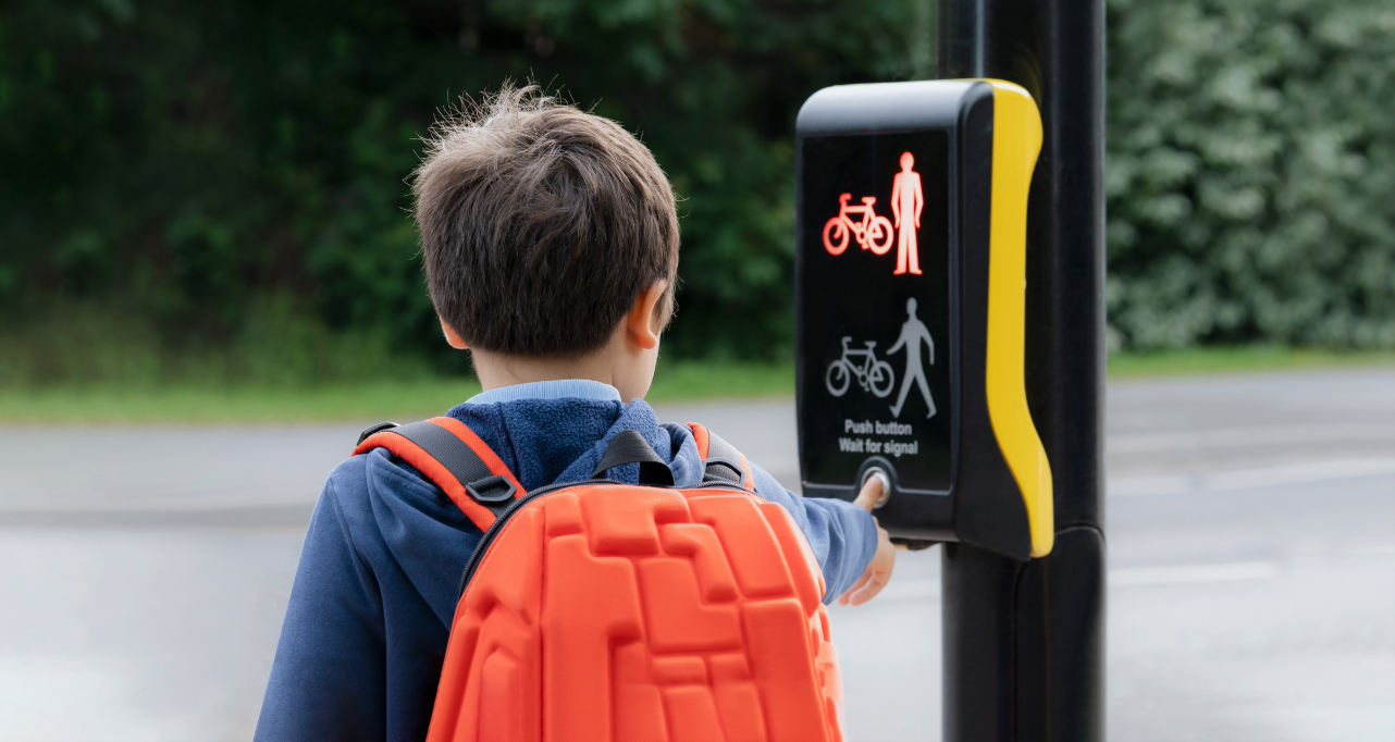 School kid pressing a button at traffic lights on pedestrian crossing on way to school